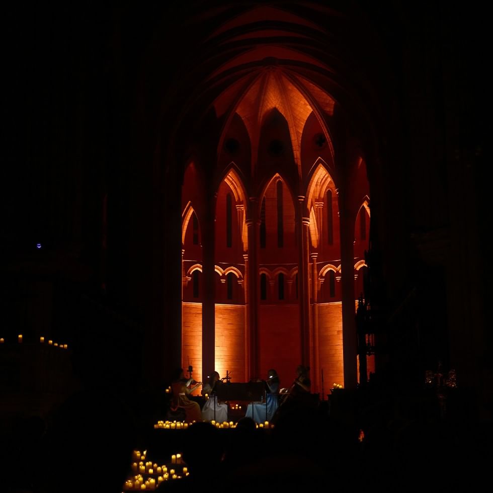 Gedimmtes Bild einer Kapelle mit Musikern vor dem Hintergrund beleuchteter Bögen bei ADVENTSKONZERTE 2025.
