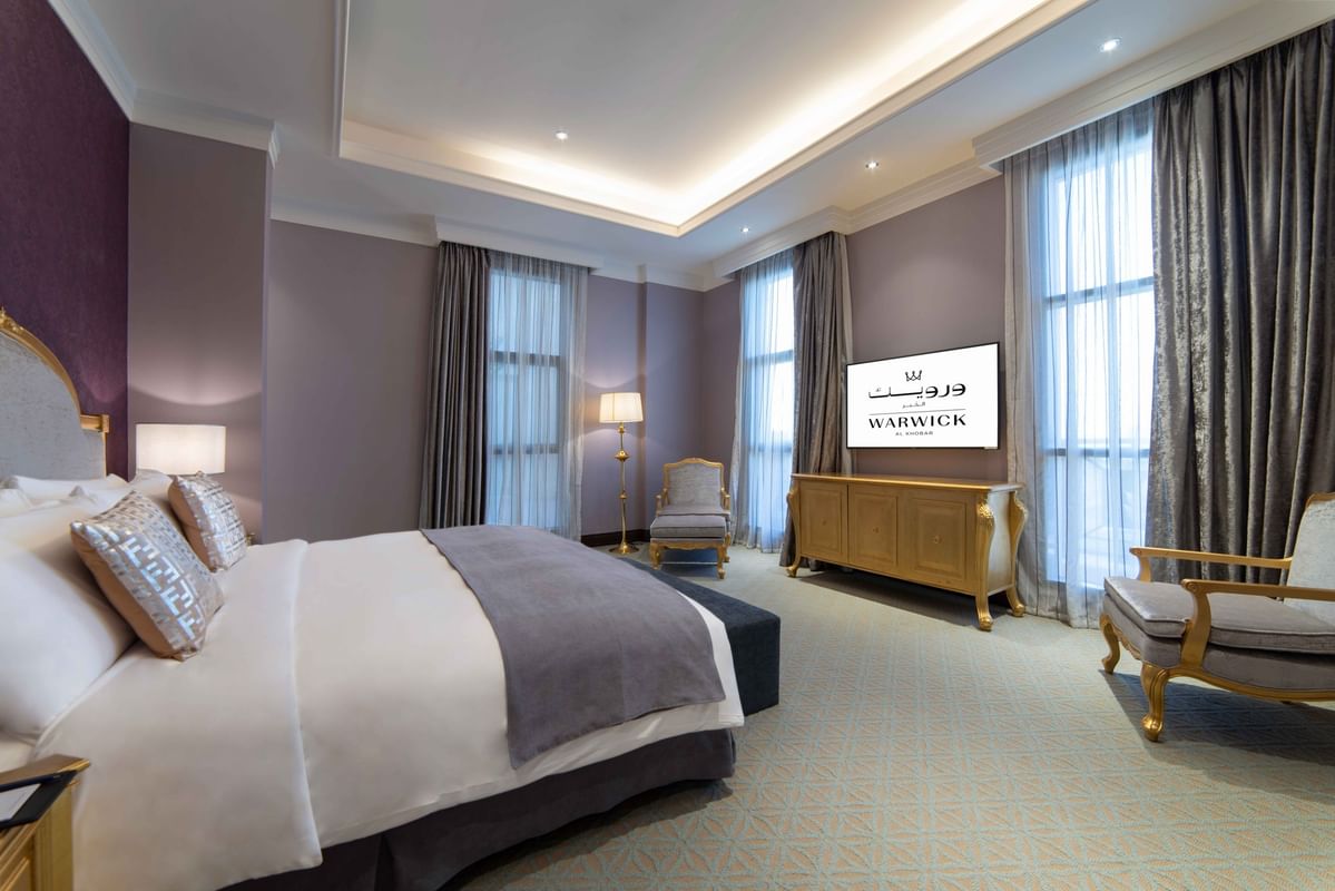 Gilded console table by a plush armchair under purple accent walls & Double bed in Penthouse Villa at Warwick Al Khobar