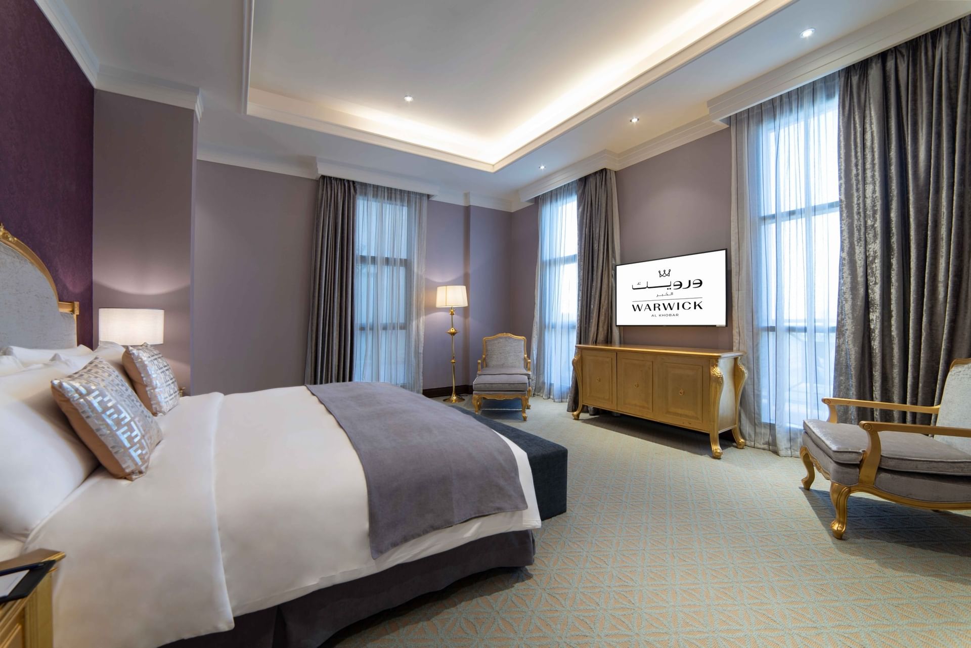 Gilded console table by a plush armchair under purple accent walls & Double bed in Penthouse Villa at Warwick Al Khobar