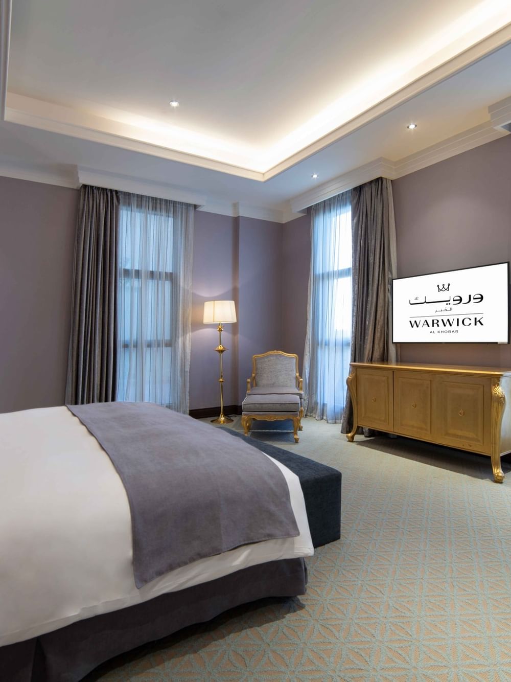 Gilded console table by a plush armchair under purple accent walls & a double bed in Penthouse Villa at Warwick Al Khobar