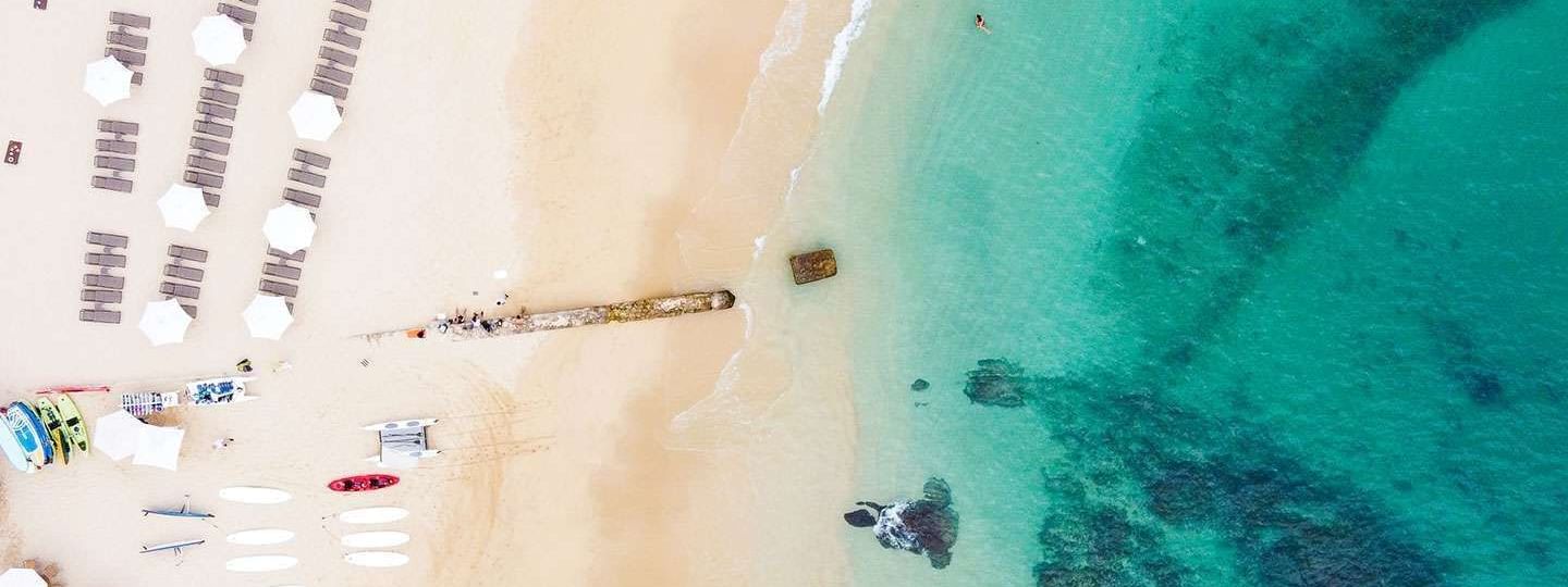 Overhead view of a sandy beach with umbrellas, and clear turquoise ocean near Marquis Los Cabos Resort