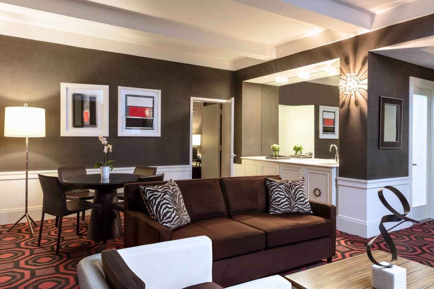 A wide view of a living room with a brown couch, a dining table, and a kitchenette.