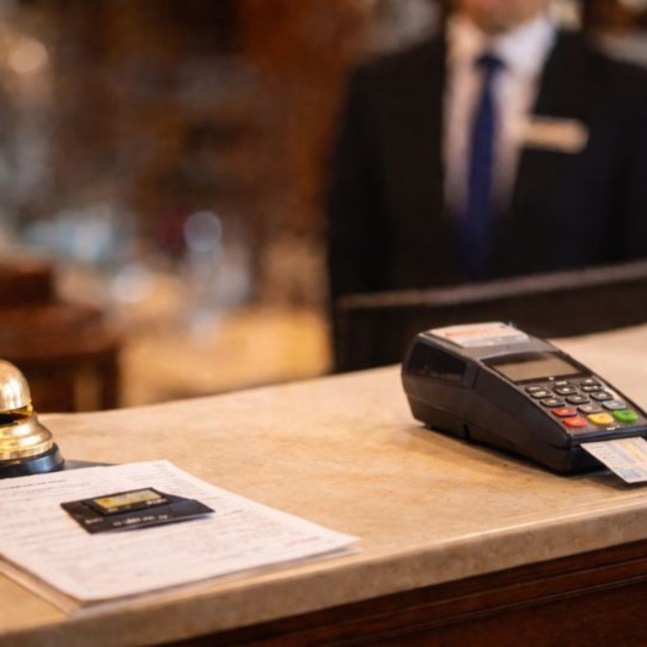 Hotel reception desk with bell, payment terminal, and papers.