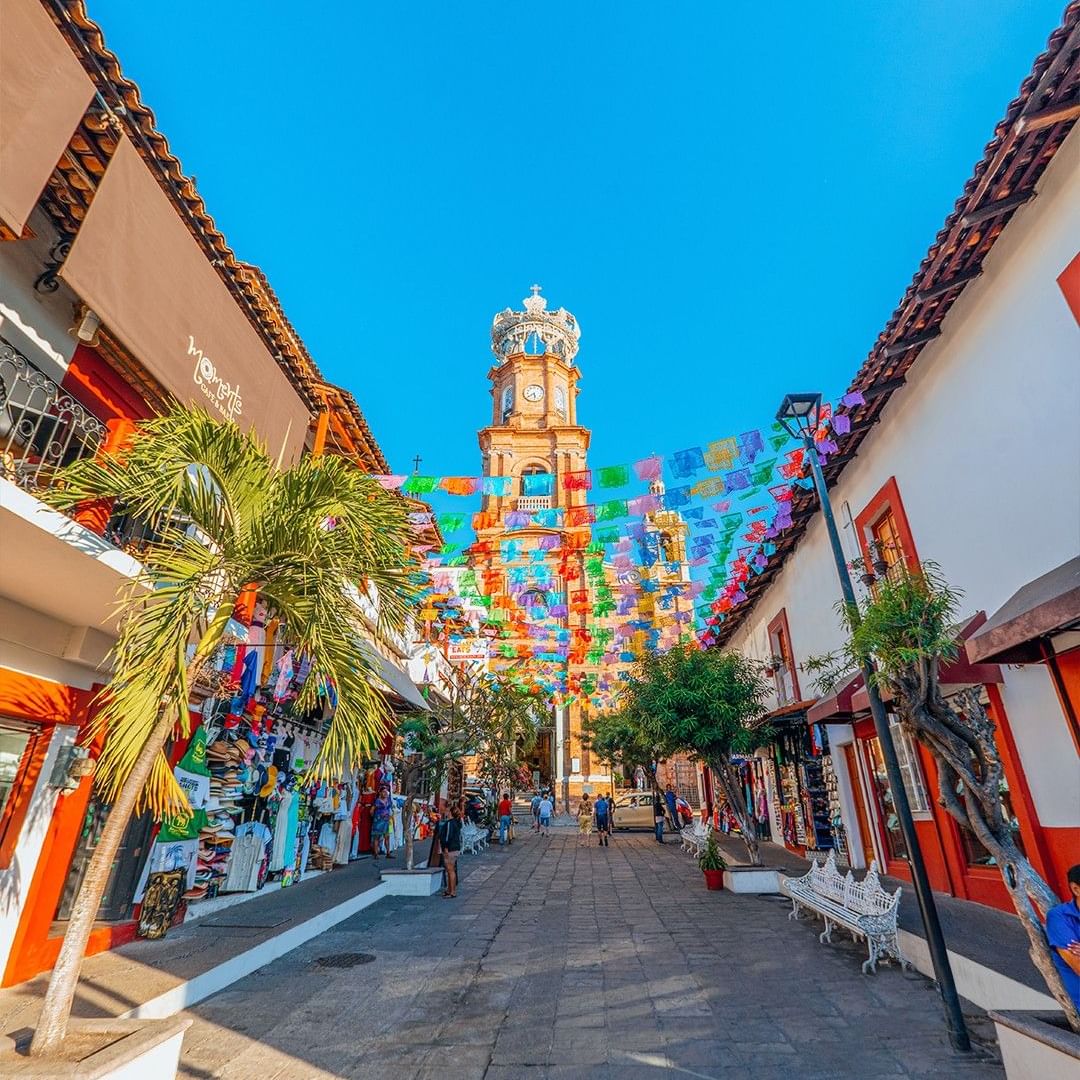 Colorful street with clock tower and shops under a blue sky in Puerto Vallarta.
