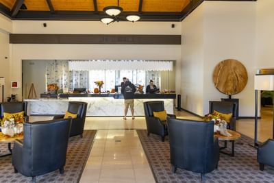 Black armchairs by a long marble desk under a high ceiling, with guests in the lobby at Rodd Miramichi River