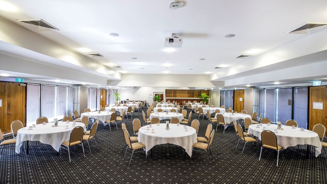 Ballroom arranged with cabaret table set and chairs, and a projector at Mercure Hotel Townsville