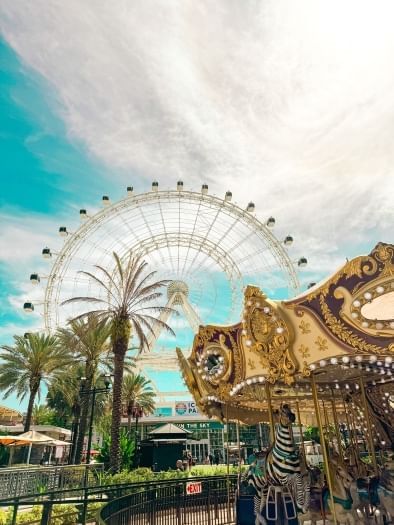 A tall ferris wheel behind palm trees with an ornate carousel in the foreground. A ride on the Orlando Eye is a great romantic date in Orlando.