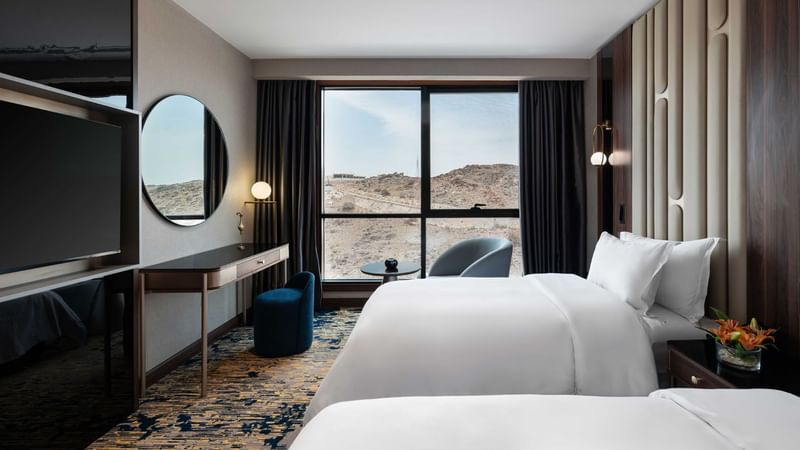TV facing two beds and rocky mountainous landscape view in Royal Suite at Warwick Hotels & Resorts