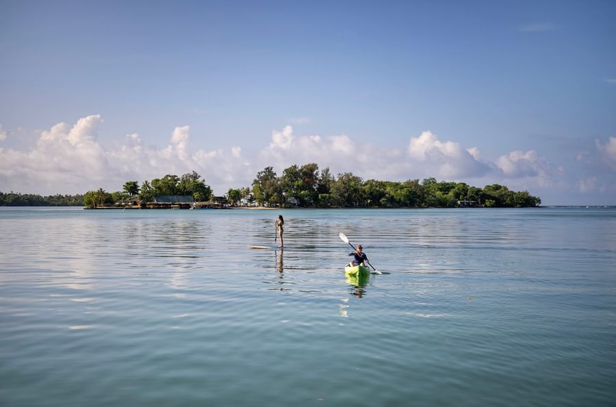 People kayaking and paddleboarding on calm waters with distant island at Warwick Le Lagon - Vanuatu.