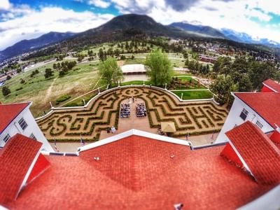 An aerial view of The Stanley Hotel, showing the red roofs, a hedge maze in the courtyard, and the mountains in the distance