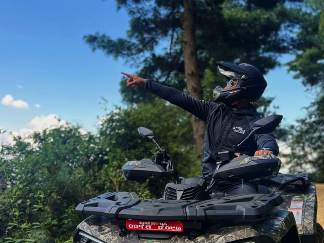 Rider in helmet on ATV pointing skyward with greenery backdrop near The Terraces Resort & Spa