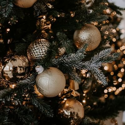 Nahaufnahme eines Weihnachtsbaums mit goldenen Kugeln und Lichterketten, festlich geschmückt.