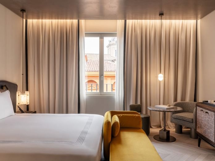 King bed room with golden velvet bench, floor-to-ceiling curtains, and city views at The Thompson Rome