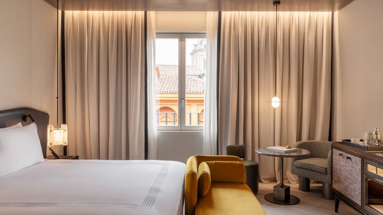 King bed room with golden velvet bench, floor-to-ceiling curtains, and city views at The Thompson Rome