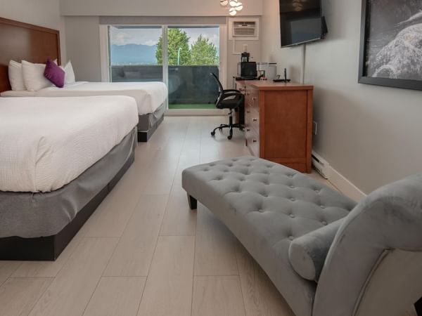 Two beds, a desk, a chair and a chaise lounge in a hotel room.