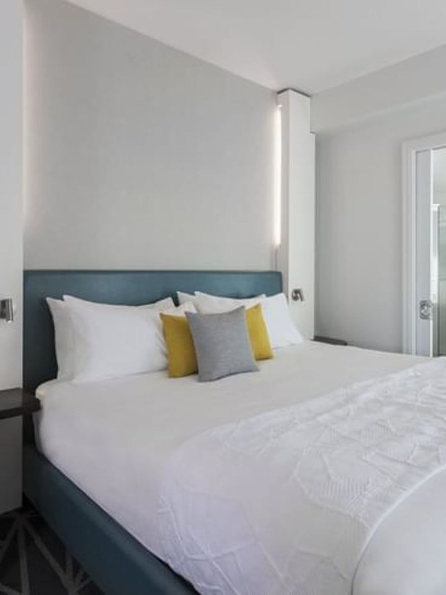 Clean white bedroom with bed and bathroom in the Penthouse René-Lévesque at Warwick Le Crystal – Montreal.