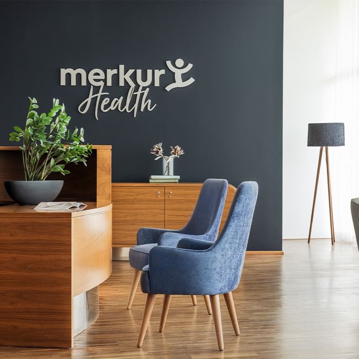 Office reception area with wooden desk, two blue chairs, a plant, and a 