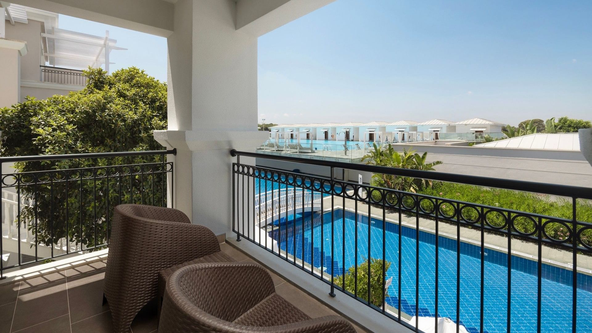 Balcony with wicker chairs overlooking a blue swimming pool and lush gardens at Titanic Deluxe Golf Belek, Antalya.