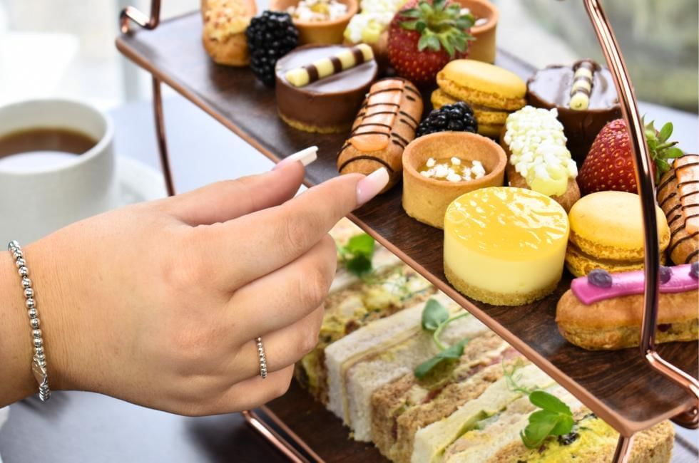 lady reaching out for a eclair on afternoon tea at gorse hill in surrey