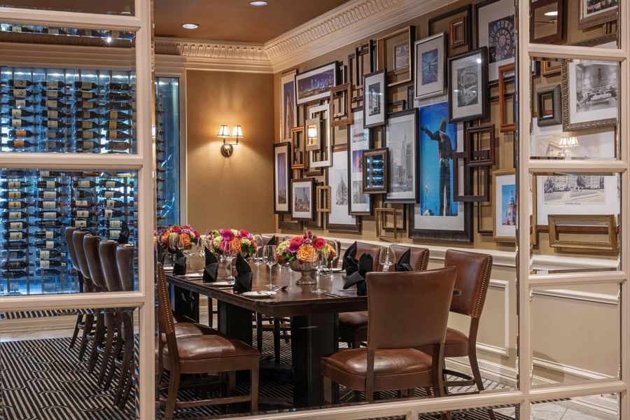 Long wood table with leather chairs by a gallery wall under warm glow lamps in Private Dining at Warwick Melrose Dallas