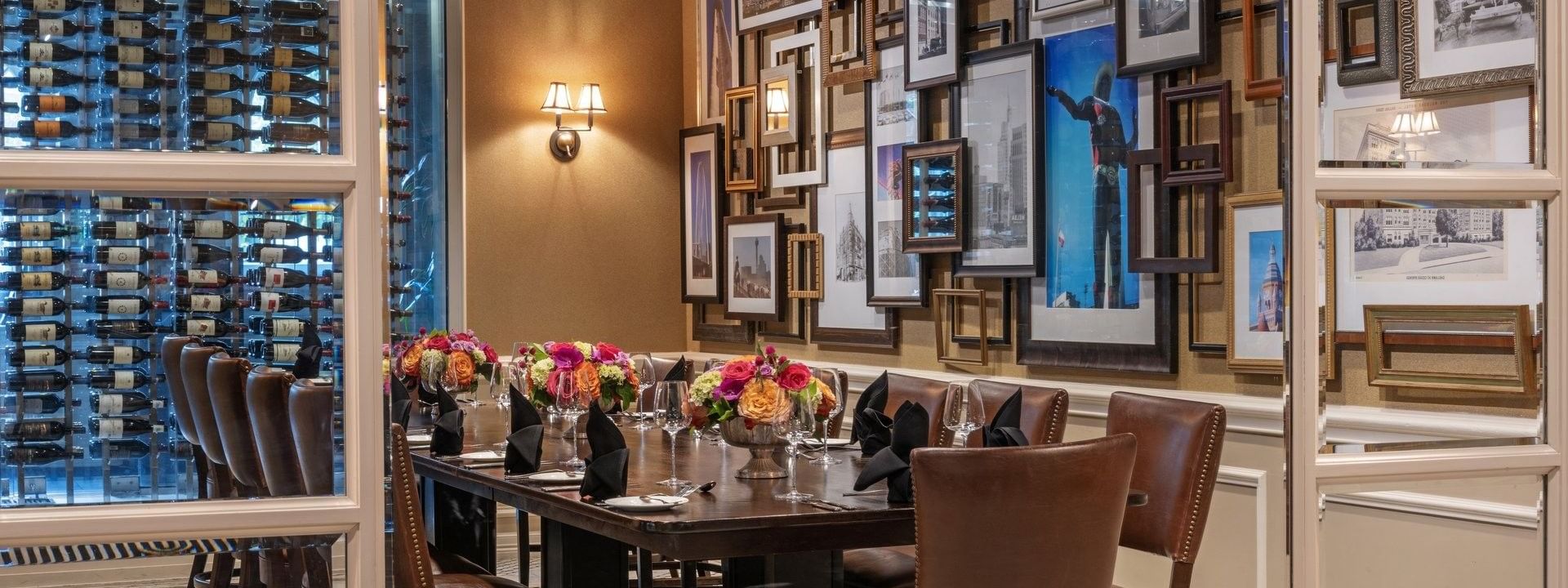Long wood table with leather chairs by a gallery wall under warm glow lamps in Private Dining at Warwick Melrose Dallas