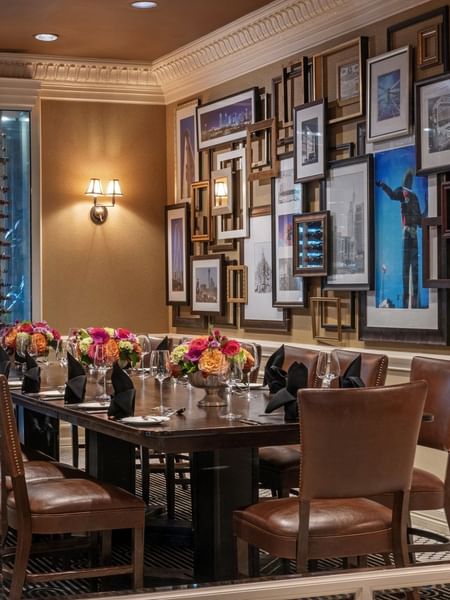 Long wood table with leather chairs by a gallery wall under warm glow lamps in Private Dining at Warwick Melrose Dallas