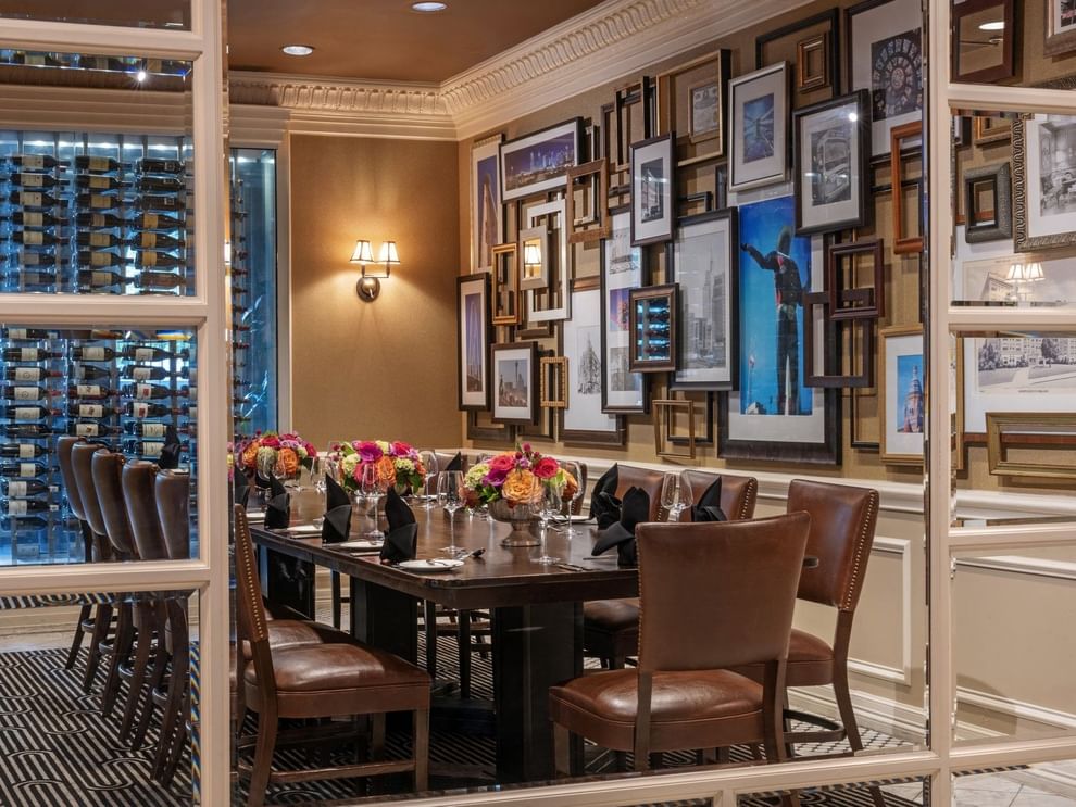 Long wood table with leather chairs by a gallery wall under warm glow lamps in Private Dining at Warwick Melrose Dallas