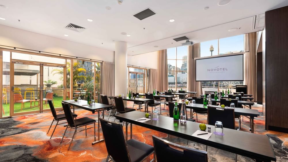 Classroom set-up with a projector screen and city view in The Hunter Room 1-4 at Novotel Sydney on Darling Harbour