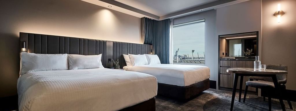 Modern superior room with two double beds, dark paneled headboards, work desk, and city views at Pullman East Melbourne.