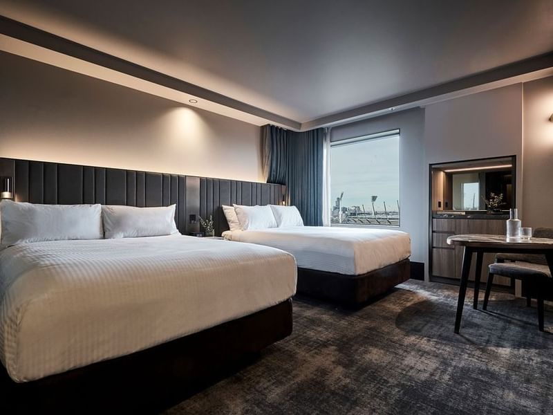 Modern superior room with two double beds, dark paneled headboards, work desk, and city views at Pullman East Melbourne.