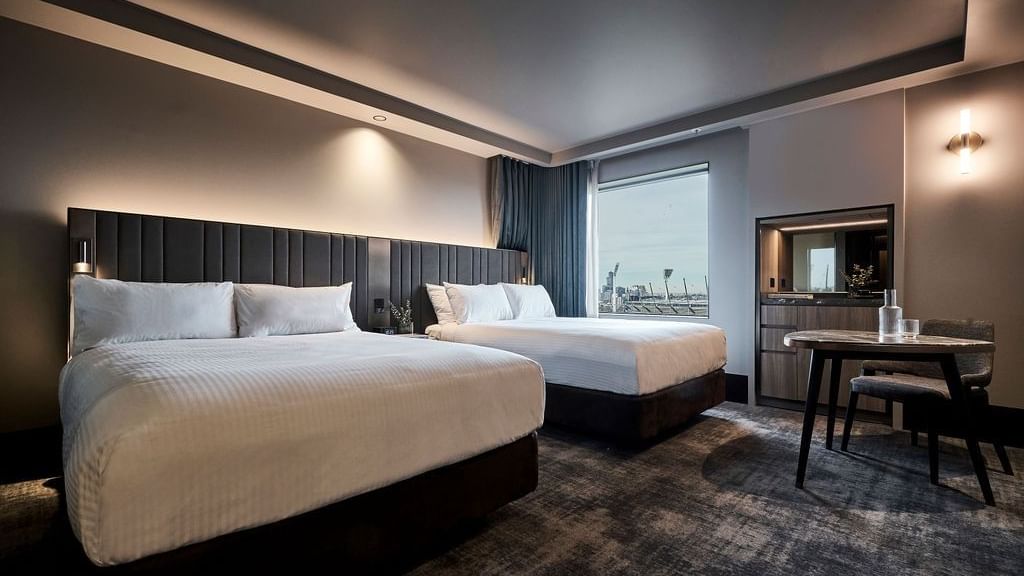 Modern superior room with two double beds, dark paneled headboards, work desk, and city views at Pullman East Melbourne.