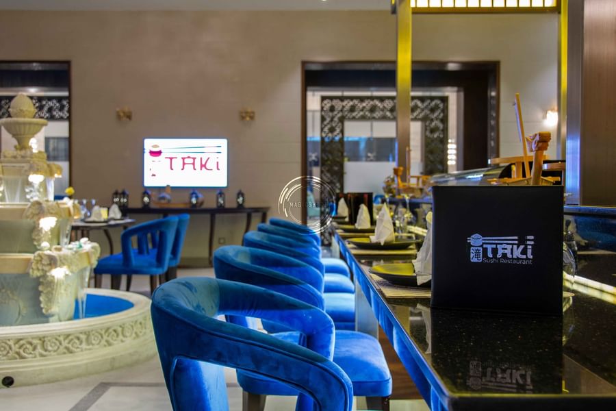 Blue velvet chairs by a long sushi counter under a glowing in Taki Restaurant at Warwick Al Khobar