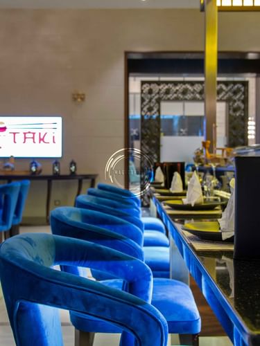 Blue velvet chairs by a long sushi counter under a glowing in Taki Restaurant at Warwick Al Khobar