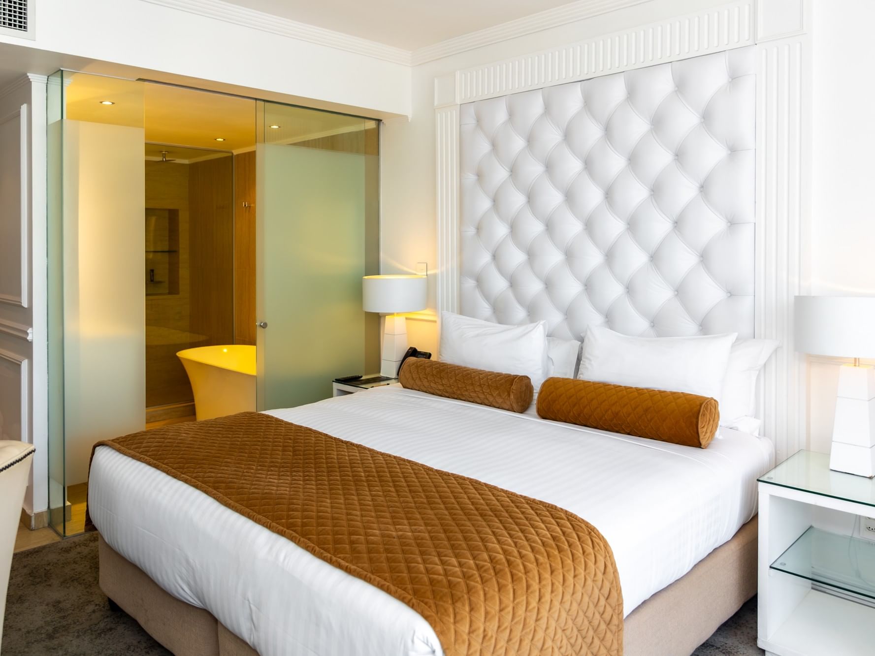 Deluxe Studio with white tufted headboard, gold accent pillows, and modern glass bathroom at Pepperclub Hotel Cape Town