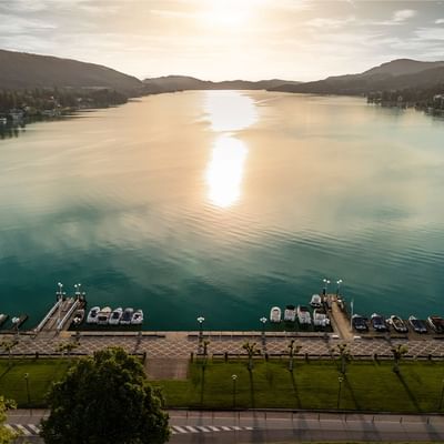 Luftaufnahme eines Sees mit Booten am Ufer und der Sonne, die über den Bergen untergeht.