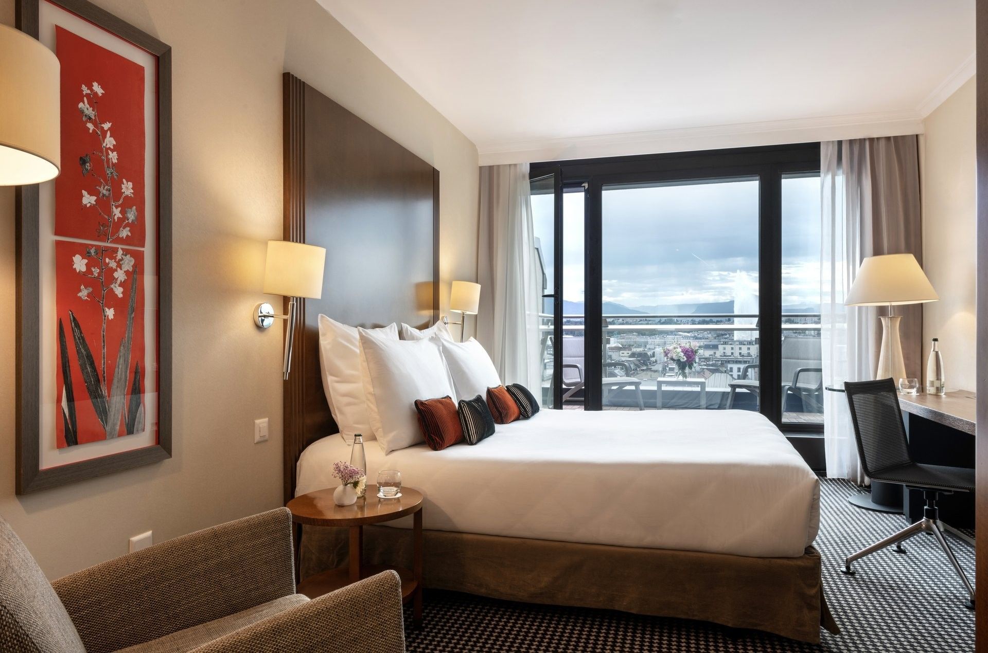 Bed by a red floral painting with pillows under warm wall lamps in Penthouse Terrace Room at Warwick Geneva