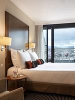 Bed by a red floral painting with pillows under warm wall lamps in Penthouse Terrace Room at Warwick Geneva