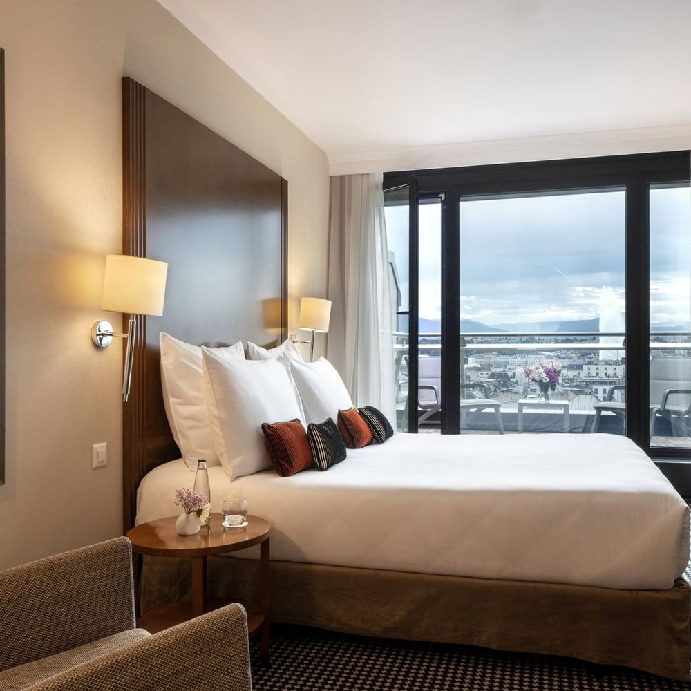 Bed by a red floral painting with pillows under warm wall lamps in Penthouse Terrace Room at Warwick Geneva
