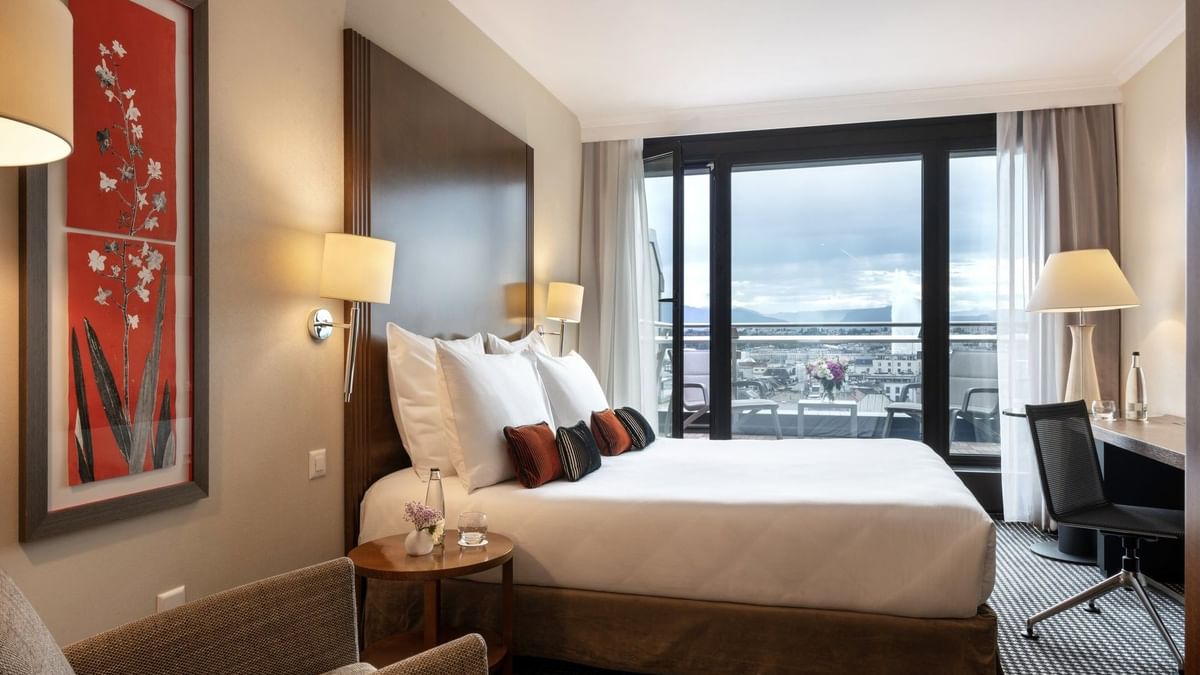 Bed by a red floral painting with pillows under warm wall lamps in Penthouse Terrace Room at Warwick Geneva