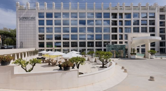 Modern office building with outdoor seating area, umbrellas, and trees in front under a clear blue sky.