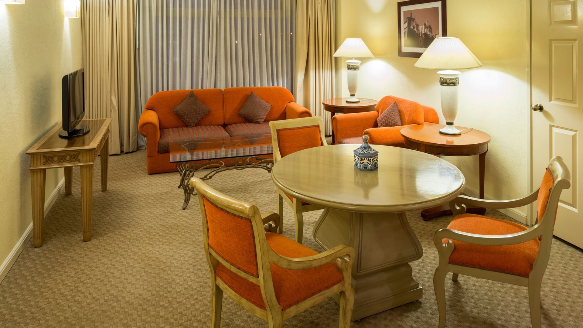 Amplia sala de estar con sofá naranja, mesa de comedor y lámparas en Camino Real Puebla Angelópolis