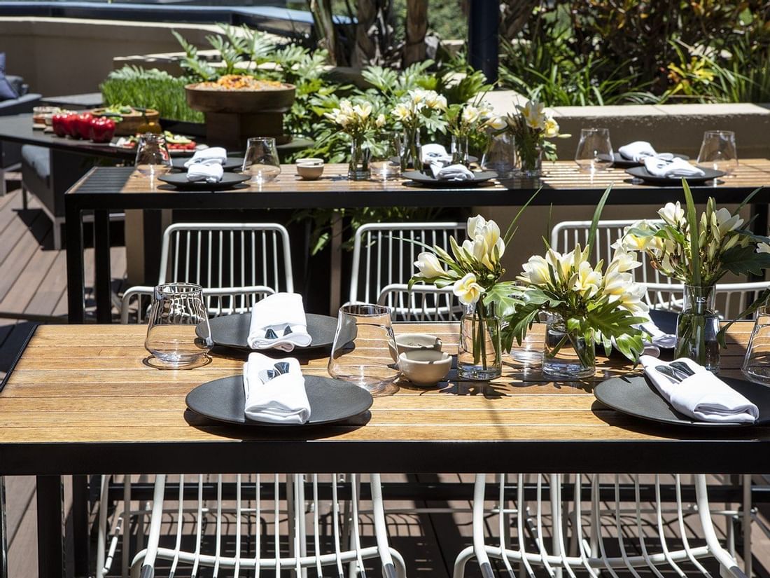 Stylish outdoor dining table set with black plates and white flowers for a sunny al fresco meal at The Sebel Brisbane