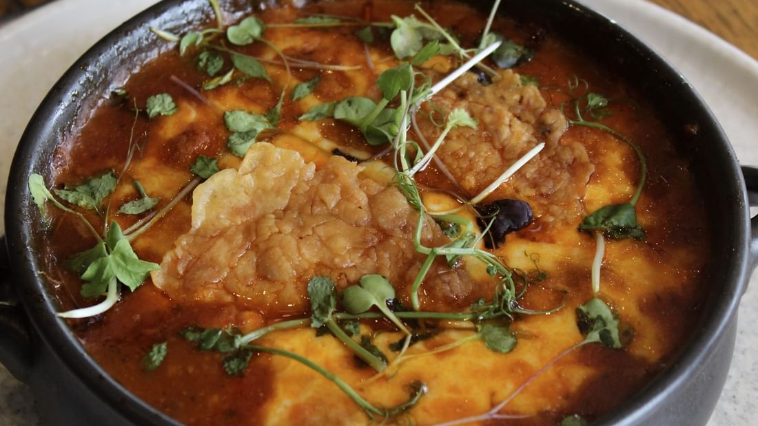 Bowl of creamy soup with meat and herbs on a plate with a fork.