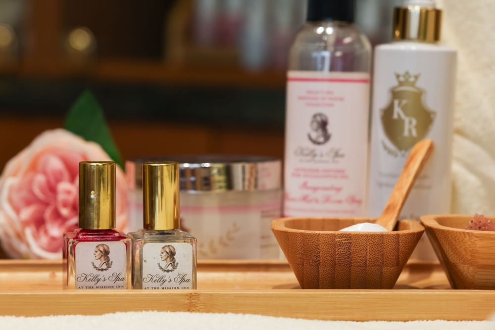 Collection of Kelly's Spa essential oils and beauty products on a wooden tray with a pink flower at Kelly's Spa