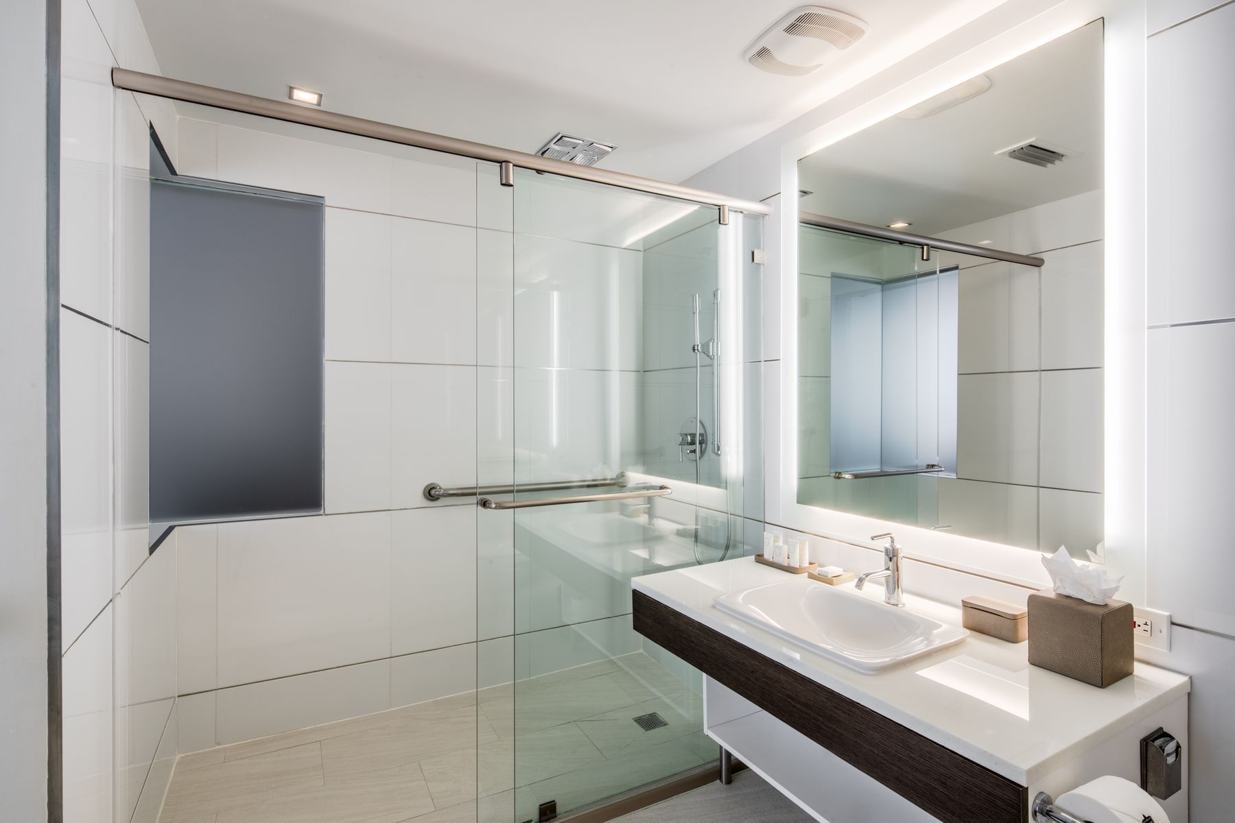 A modern bathroom with a glass-enclosed shower, a white sink, and a large mirror.