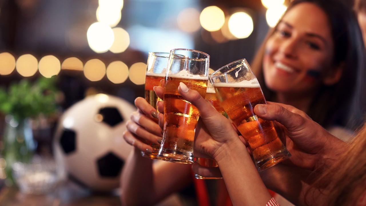 Four beer glasses clinking together with a soccer ball in the background