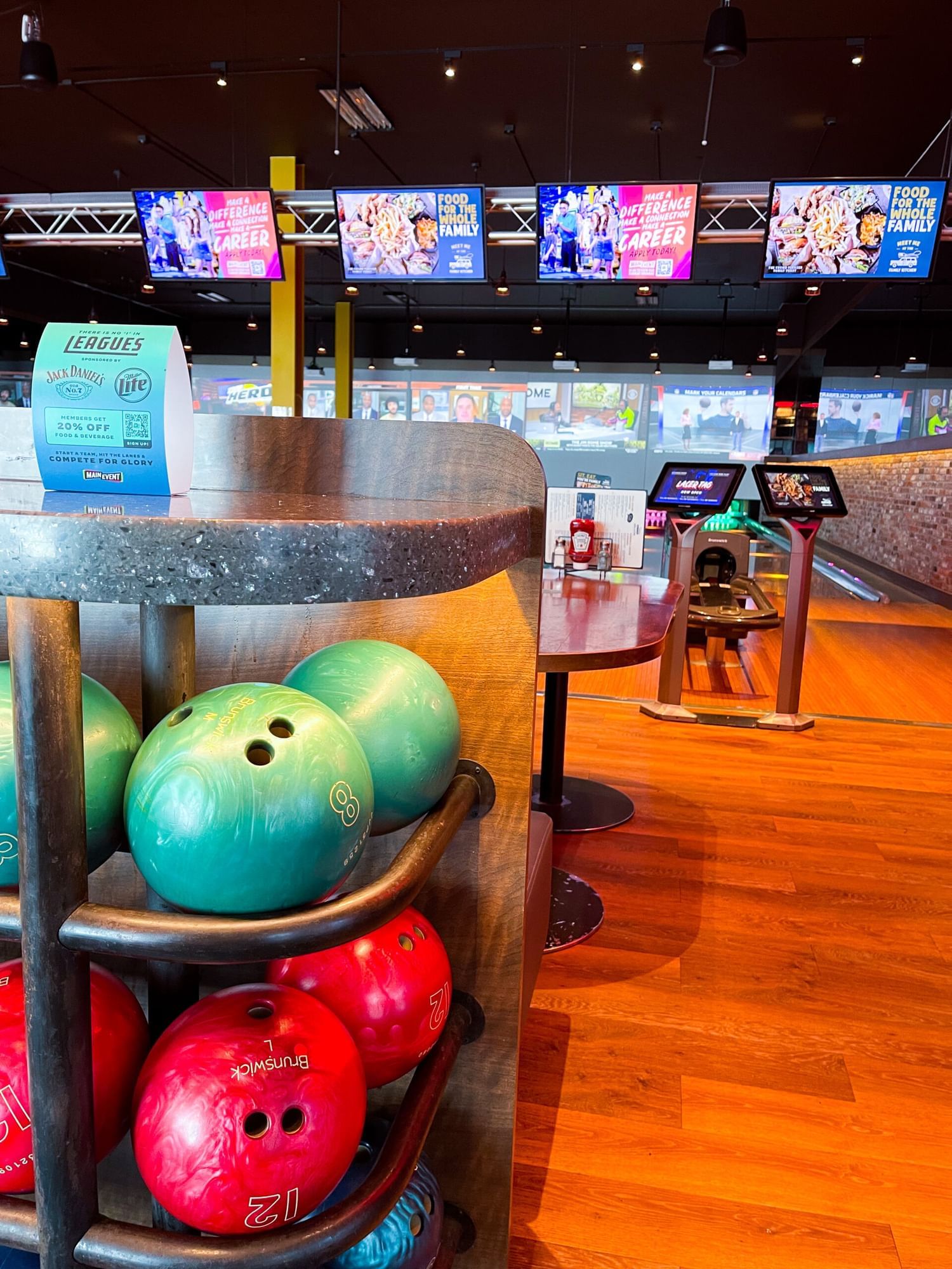 A shelf of colorful bowling balls overlooking bowling alleys with large screens.
