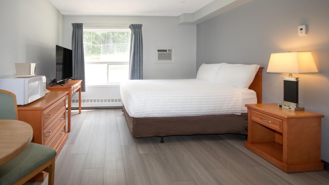 Hotel room with bed, dresser, microwave, TV, window, and two wooden nightstands with lamps.