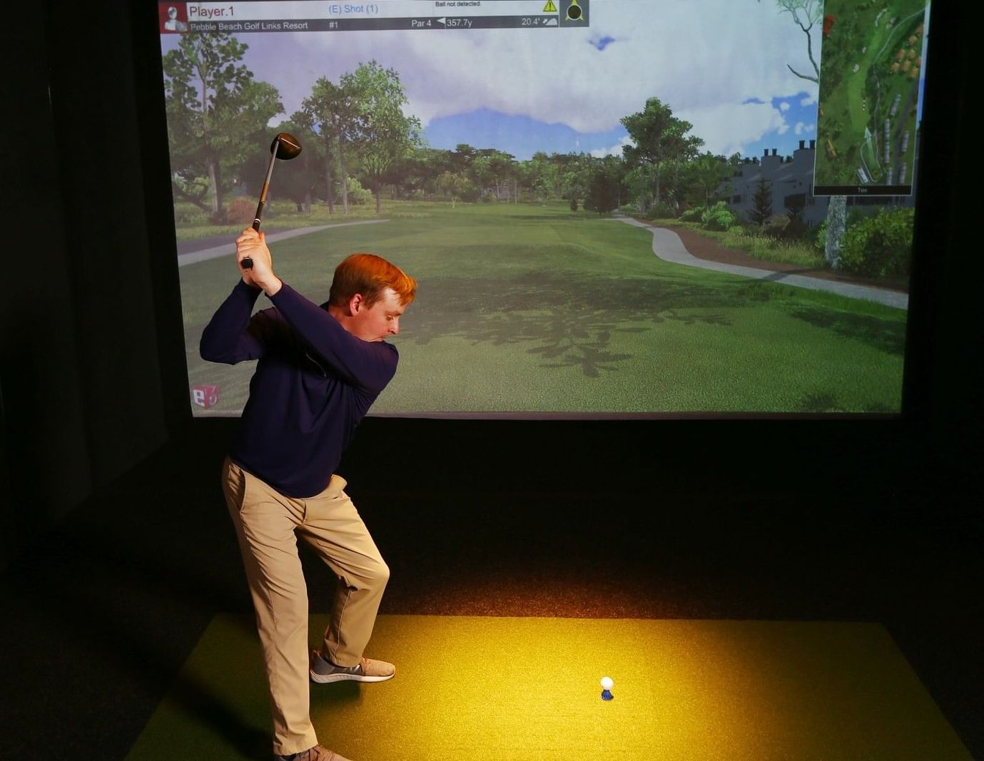 Man swinging a golf club on an indoor golf simulator with a projected course display at Hotel X Toronto