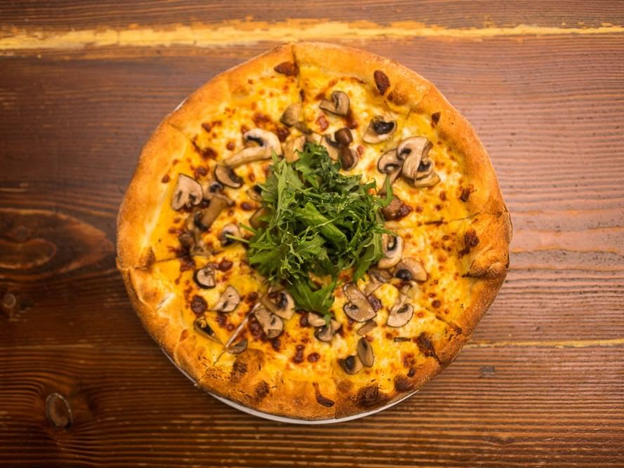 Pizza topped with mushrooms and arugula on a wooden table at Pickwick San Francisco.